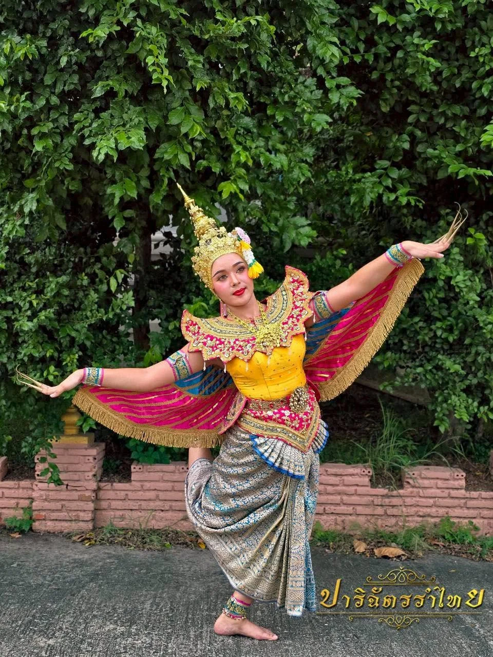 ผู้แสดงชุดสีเหลืองพร้อมปีกกางแขนในท่ารำ